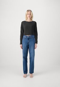 Zwarte geribbelde cropped trui met lange mouwen, gecombineerd met blauwe wijde jeans. Model draagt beige bandjesandalen. Zachte texturen en casual pasvorm.