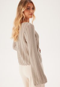 Maglione beige a maglia con texture a coste, maniche lunghe e vestibilità rilassata, caratterizzato da cuciture aperte e orlo corto sul retro.