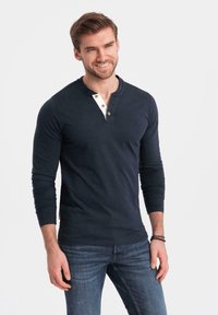 Marineblauwe lange mouwen Henley-shirt met een witte bies en drie tan knopen, gecombineerd met blauwe denim jeans, met een ontspannen pasvorm.