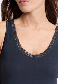 Canottiera blu scuro con una profonda scollatura a V e un delicato bordo in pizzo. Realizzata in tessuto morbido e liscio, offre una silhouette aderente.