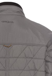 Graue gesteppte Jacke mit hohem Kragen, schwarzen Akzenten und "camel active"-Logo. Auffällige Nähte und strukturierter Stoff sichtbar.