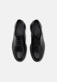 Chaussures habillées en cuir noir avec une finition lisse, design à lacets, bout rond et semelle plate. Comprend un branding subtil sur la semelle intérieure.