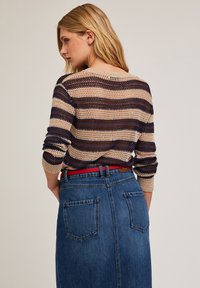 Gestreifter Strickpullover in Beige, Marineblau und Rost, mit lockerer Passform und Rundhalsausschnitt, kombiniert mit einem knielangen Jeansrock mit hinteren Taschen.