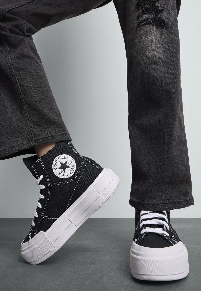 Sorte canvas høyhælte sneakers med hvit gummisåle og sømmer. Har Converse All Star-logo på siden. Brukt med svarte slitte jeans.