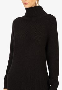 Schwarzer gerippter Rollkragenpullover mit langen Ärmeln, mit einem hohen Kragen und einer weichen, strukturierten Oberfläche.