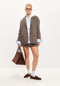 Brown wool blazer over a light blue shirt, paired with a matching brown skirt and brown suede loafers. Holding a brown suede bag.