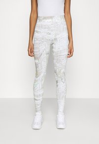 Leggings med ett reflekterande, virvlande vitt mönster och hög midja. Tillverkade av stretchigt, lätt material och kombinerade med vita sneakers.