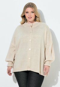 Cardigan beige con bottoni, collo alto, polsini a coste e vestibilità rilassata, realizzato in morbido tessuto lavorato a maglia. Decorato con grandi bottoni.