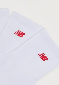 Δύο ζεύγη λευκών αθλητικών κάλτσων με κόκκινα κεντημένα λογότυπα "NB" σε λευκό φόντο.