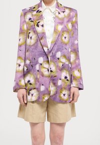Blazer con estampado floral en púrpura, con mangas abullonadas de gran tamaño, solapas de muesca y dos bolsillos frontales, acompañado de pantalones cortos beiges.