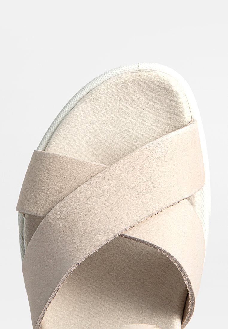 Beige Kreuzriemensandale mit Obermaterial aus strukturiertem Leder und einer weißen Gummisohle, die klare Linien und ein minimales Design betont.