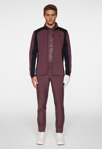 Bordeaux och svarta sportkläder, som inkluderar en jacka med dragkedja, ett mönstrat underställ och matchande byxor; inkluderar vita handskar och skor.