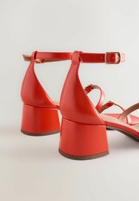 Røde faux læder sandaler med blokhæle, ankelrem og krydset frontdesign. Glat tekstur og en bred, robust hæl.