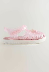 Sandale pour enfant translucide rose pailletée avec une semelle blanche et une décoration florale sur la bride avant, vue de côté.