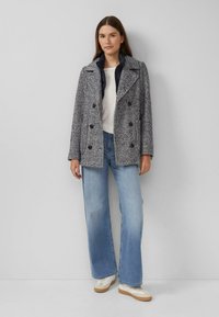 Płaszcz peacoat w jodełkę w kolorach granatowym i białym, z dużymi czarnymi guzikami, kołnierzem z wycięciami i skośnymi kieszeniami. Noszony z jeansami o rozszerzanych nogawkach.