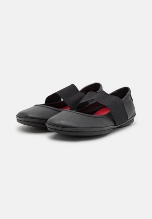 Zapatos de cuero negro con suela plana, punta redondeada y banda elástica ancha en el empeine. El interior cuenta con un forro rojo.