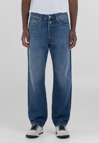 Un jean en denim bleu clair avec une coupe décontractée, présentant une jambe droite, cinq poches et des détails de couture visibles. Stylé avec des baskets blanches.