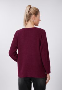 Pull texturé bordeaux à coupe ample, col large et manches longues. Caractérisé par un tissu doux et duveteux ainsi qu'un ourlet bas au dos.