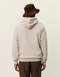 Beige színű, kapucnis pulóver, puha textúrával, lazán szabott fazonnal és bordázott mandzsettákkal, barna kordbársonykalap kiegészítve.