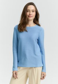 Pull bleu clair à manches longues avec texture côtel�ée, col rond et coupe décontractée, associé à un pantalon crème.
