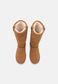Braune Wildleder-Stiefel bis zum Knie mit einem weichen, cremefarbenen Innenfutter, das ein schlichtes Design und eine Detail mit Rückenschnalle für einen sicheren Sitz aufweist.