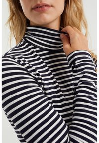 Svart- och vitrandig polokrage med långa ärmar, tillverkad av stretchigt material. Närbild som betonar kragen och ärmarnas design.