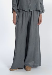 Pantaloni larghi in lino grigio, leggeri, con vita elasticizzata, abbinati a una camicia cropped con bottoni dello stesso colore e espadrillas in paglia color sabbia.