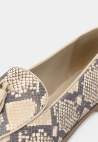 Mocassins en python avec un schéma de couleurs beige et marine, texture lisse et un détail de frange décoratif à l'avant.