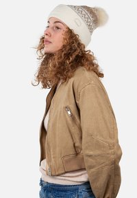 Beige bomberjack met ribbelmanchetten, ritszakken en een gestructureerde stof. Gedragen met een licht sweater en een crème-gepatenteerde gebreide muts.