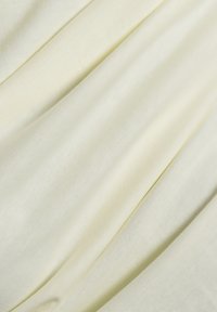 Helles gelbes Gewebe mit einer glatten, leicht strukturierten Oberfläche, das sanfte Drapierungen und sanfte Falten aufweist, die Flexibilität und Komfort anzeigen.