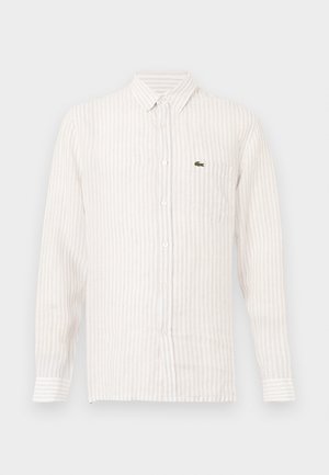 Világos színű, csíkos ing hosszú ujjal, gombos nyakkal, és egy kis zöld logóval a bal oldali zseben. Pamut anyag.