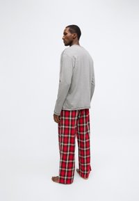 Pelēka ar garām piedurknēm krekls kopā ar sarkaniem un melniem pleda raksta mājas džinsiem. Audums izskatās mīksts; bikses ir brīvas pieguļas un ar nelielu platumu pie potītēm.