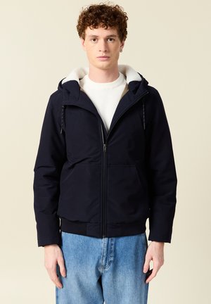 Navyblauwe hoodie met rits aan de voorkant, gevoerd met fleece bij de kraag en elastische manchetten, gecombineerd met lichtblauwe jeans.