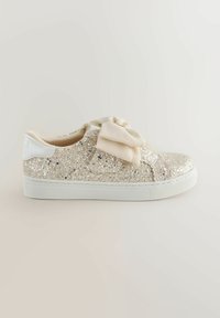 Sneaker beige scintillante a taglio basso con suola bianca e grande fiocco in tessuto morbido sopra, mostrato dal lato esterno.