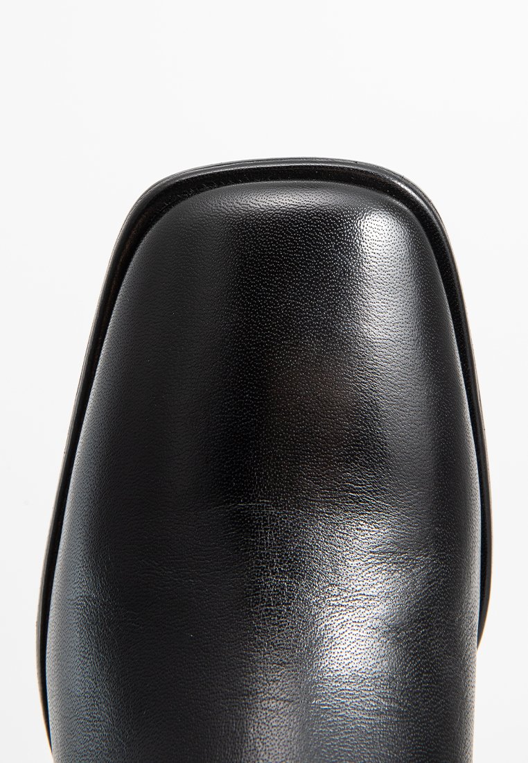 Scarpa quadrata in pelle nera lucida vista dall'alto su sfondo bianco.