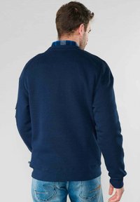 Felpa blu navy con texture a coste, scollo rotondo e maniche lunghe; particolare colletto a quadri sovrapposto visibile sul retro.
