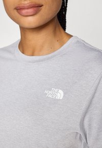 Lichtgrijze t-shirt met korte mouwen, voorzien van een geribbelde textuur en een wit logo-ontwerp van "The North Face" op de linkerbovenkant.