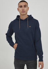 Marineblaues Hoodie mit einer Kängurutasche, Kapuze mit Kordelzug und geflochtenen Akzenten sowie einem kleinen Logo-Patch auf der Brust.