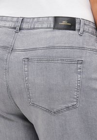 Gray denim jeans feature a standard back pocket design and a branded black leather patch at the waistband. Smooth texture, classic fit.