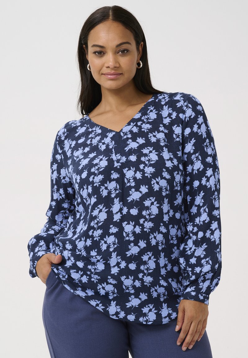 Blusa azul marino con patrón floral en azul claro, escote en forma de V y mangas largas. Tejido ligero y texturizado. Combinada con pantalones marinos.