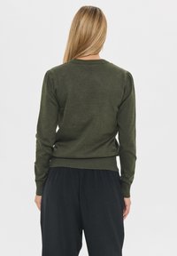 Suéter verde de punto con mangas largas, dobladillo acanalado y pliegues en los hombros. La tela texturizada tiene un acabado suave contra un fondo claro.