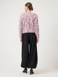 Πλεκτή ροζ και λευκή ζακέτα με υφασμένο σχέδιο, συνδυασμένη με φαρδιά μαύρη παντελόνα. Το μοντέλο φοράει μαύρα παπούτσια με τακούνι.