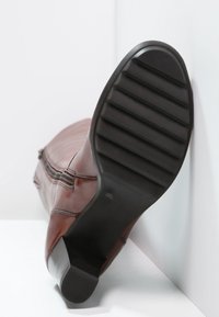 Bota alta hasta la rodilla de cuero marrón con suela de goma negra texturizada, con detalle de cremallera a lo largo del lateral. Acabado liso, diseño aerodinámico.