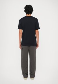 Camiseta de algodón negra con mangas cortas, corte relajado y escote redondo. Combinada con pantalones cargo gris con bolsillos laterales y una silueta holgada.