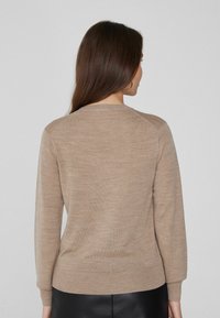 Suéter de punto marrón claro con cuello redondo y mangas largas. Presenta un dobladillo ajustado y una textura suave, con detalles de mangas raglán.