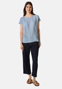 Lichtblauw linnen shirt met opgerolde korte mouwen, gecombineerd met donkerblauwe wijde jeans en tan kleurige sandalen met banden. Soepele textuur, casual ontwerp.