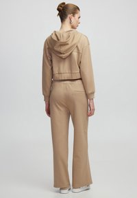 Beige cropped hoodie met een koord, gecombineerd met wijde broeken. Gemaakt van zachte stof, met elastische boorden en een achterzak.
