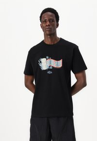 Zwarte katoenen T-shirt met een kleurrijk grafisch ontwerp, met de tekst "Santa Cruz", een tribale masker en palmbomen accent op de voorkant.