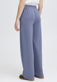 Pantalon large en tissu doux et texturé de couleur bleu clair. Doté d'une taille élastique et d'une coupe décontractée, associé à des chaussures foncées.
