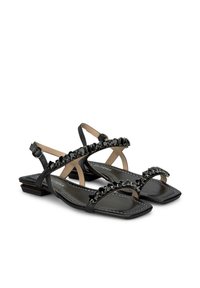 Sandalias planas negras con un acabado brillante, que presentan tiras cruzadas y gemas decorativas negras en la parte superior, plantillas texturizadas y pequeños tacones cuadrados.
